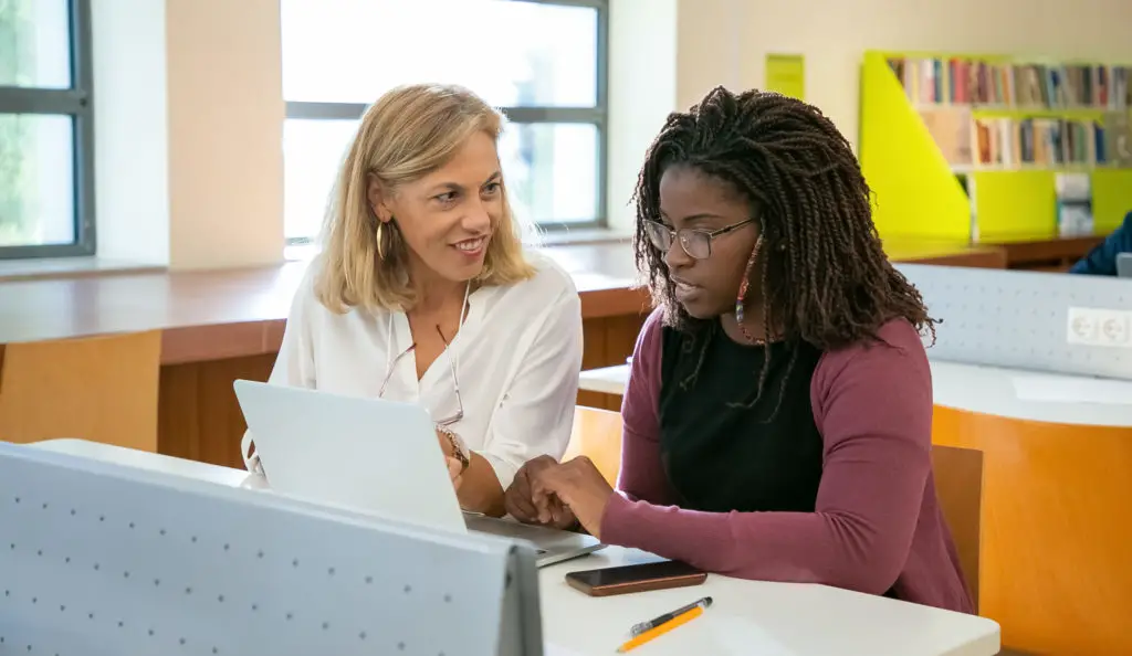 Young ethnic female student doing assignment with tutor in university