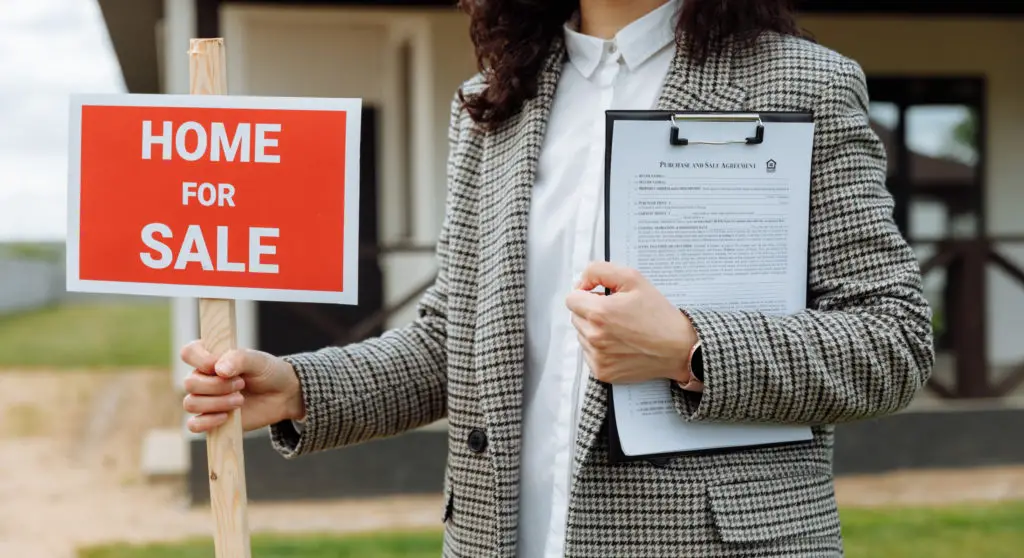 Close up of a woman holding a home for sale sign